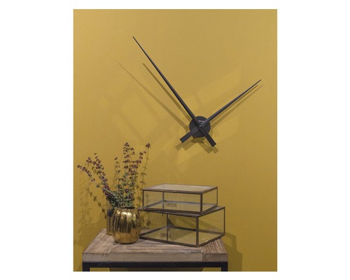 Dekoratívna scéna s nástennými hodinami, zlatým kvetináčom a sklenenými krabicami na stole.