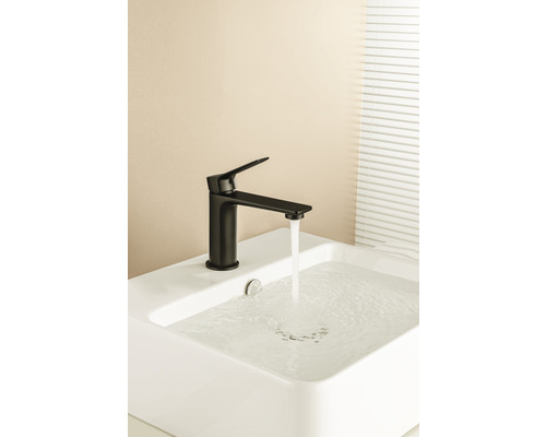 Čierna armatúra na bielom umývadle s tečúcou vodou.