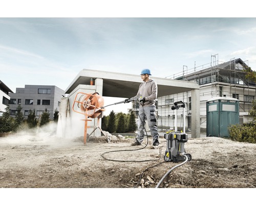 Muž čistí miešačku betónu vysokotlakovým čističom na stavenisku.