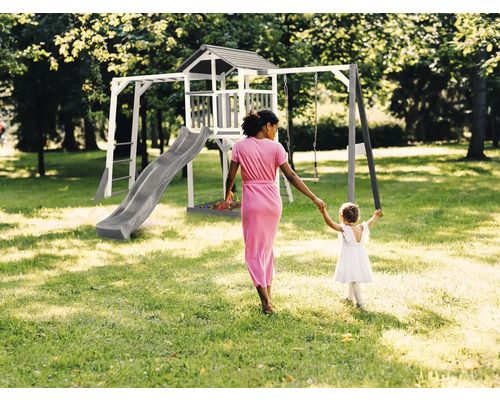 Ihrisko s hojdačkou, šmýkačkou a herným domčekom v záhrade. Žena drží dieťa za ruku.
