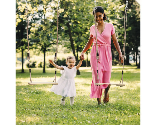Matka a dcéra sa hrajú na drevenej hojdačke v parku.