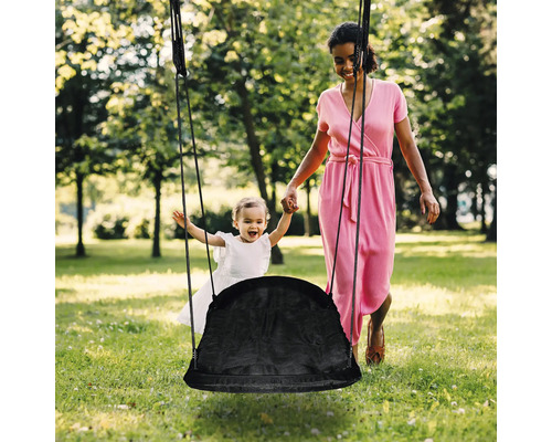 Žena hojdá dieťa na hniezdovej hojdačke v záhrade.