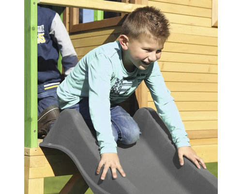 Chlapec sa kĺže na šedej šmýkačke na hracej veži.