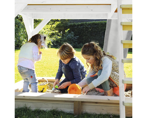 Deti sa hrajú v pieskovisku so strechou a rebríkom v záhrade.
