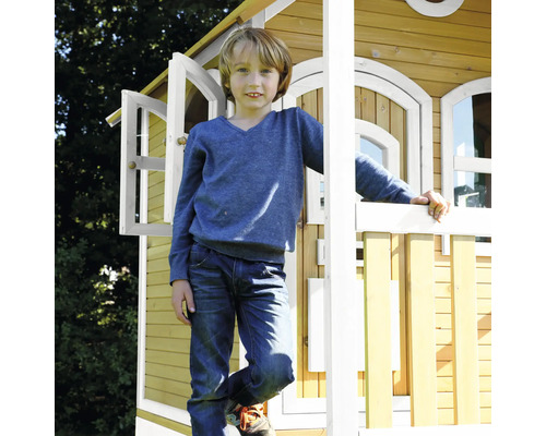 Chlapec stojí pred dreveným hracím domom s otvorenými oknami