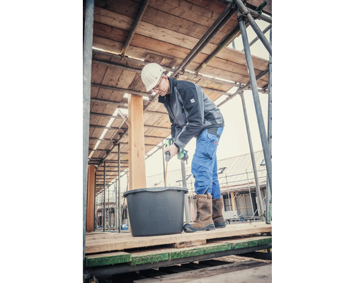 Remeselník mieša maltu s elektrickým miešadlom na lešení.