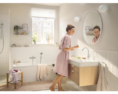 Svetlá kúpeľňa s vaňou, skrinkou pod umývadlo a ženou pred zrkadlom