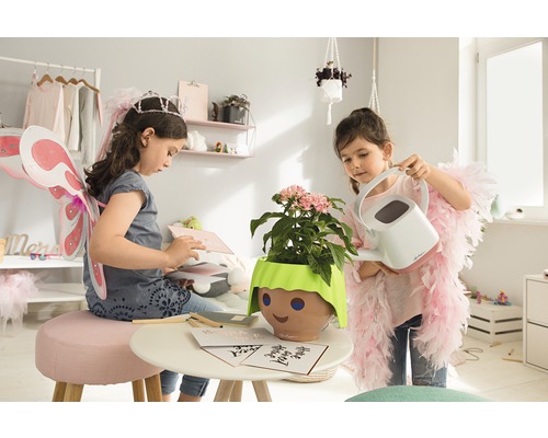 Dve dievčatá sa hrajú v izbe s rastlinou v kvetináči s tvárou a kanvou.