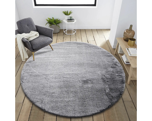 Okrúhly sivý koberec v obývacej izbe s kreslom a príručným stolíkom.