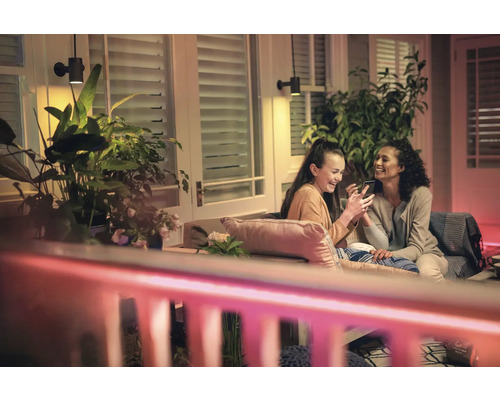 Dve ženy sedia na terase pod nástennými svietidlami a izbovými rastlinami.