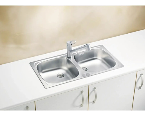 Nerezový drez s dvojitou misou a vodovodnou batériou na bielom kuchynskom stole