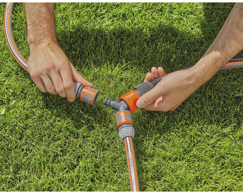 Dve ruky spájajú záhradnú hadicu s Y-rozdeľovačom na trávniku.