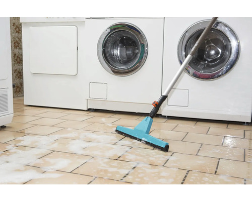 Mop so stierkou pred práčkami na dlaždenej podlahe