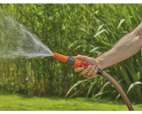 Osoba drží záhradnú hadicu so sprchovou hlavicou, z ktorej vyteká voda.
