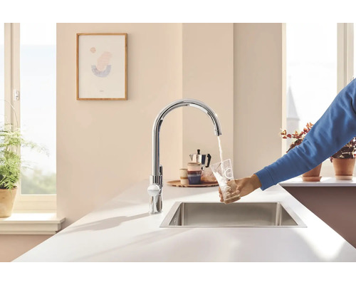 Kuchynská scéna s drezovou batériou, drezom a osobou napúšťajúcou pohár vody