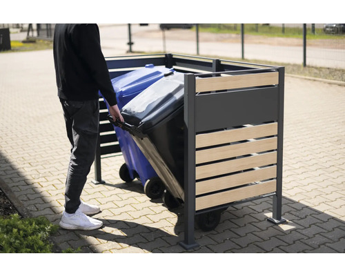 Osoba zasúva smetný kôš do kovového a dreveného boxu na smetné koše