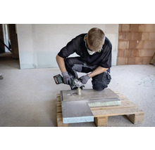 Remeselník s akumulátorovou uhlovou brúskou pri práci na doske