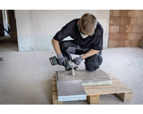 Remeselník s akumulátorovou uhlovou brúskou pri práci na doske