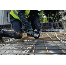 Remeselník kľačí na stavenisku a reže oceľové nosníky uhlovou brúskou Metabo, pričom lietajú iskry.