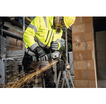 Stavebný robotník v ochrannom odeve používa uhlovú brúsku na rezanie kovu.