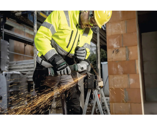 Stavebný robotník v ochrannom odeve používa uhlovú brúsku na rezanie kovu.