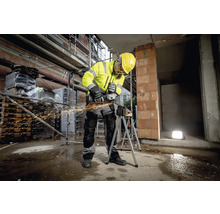 Stavebný robotník v pracovnom odeve používa uhlovú brúsku na stavenisku