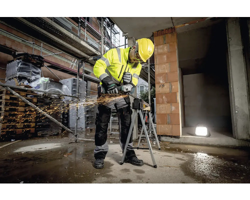 Stavebný robotník v pracovnom odeve používa uhlovú brúsku na stavenisku