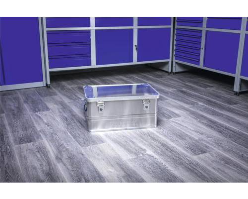Hliníkový box na náradie na podlahe dielne pred modrými skrinkami na náradie
