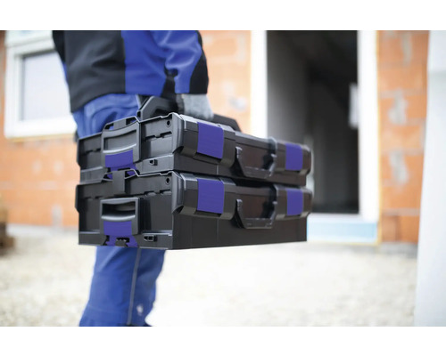 Remeselník nesie dva čierne kufríky na náradie na stavenisku