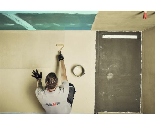 Muž valčekom nanáša farbu na stenu