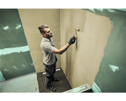 Muž maľuje valčekom stenu v kúpeľni