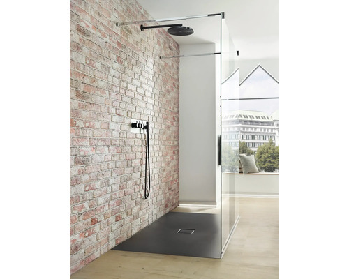 Walk-in sprcha s hlavovou sprchou, armatúrou a sprchovacou vaničkou pred tehlovou stenou
