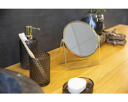 Zátišie v kúpeľni s dávkovačom mydla, pohárom na zubné kefky, zubnou kefkou, zrkadlom a miskou na mydlo na drevenom stole