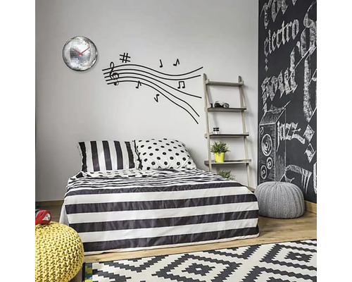 Spálňa s pruhovanou posteľnou bielizňou, nálepkou na stenu s notami a nástennými hodinami so zrkadlovými guľami