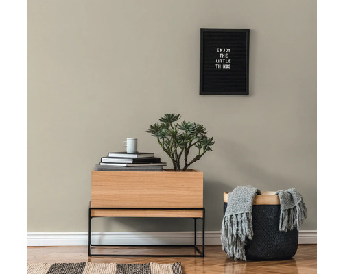 Obývacia izba s dreveným stolom, rastlinou, knihami, šálkou, košom s dekou a zarámovaným citátom na stene.