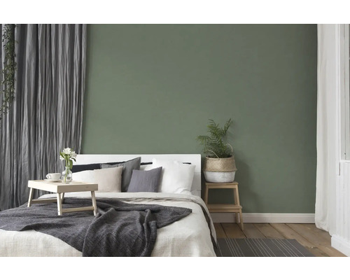 Spálňa s posteľou, nočným stolíkom a dekoráciou pred zelenou stenou