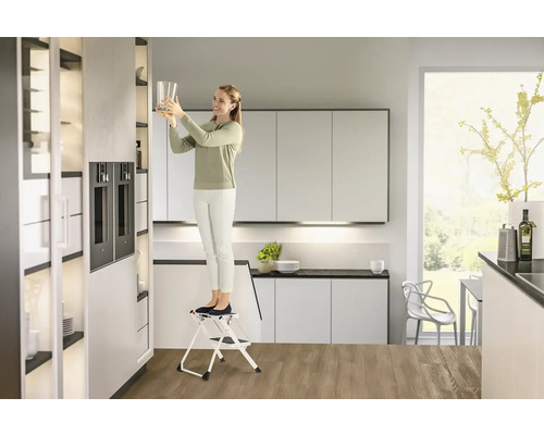 Žena na stoličke v modernej kuchyni dáva pohár do skrine