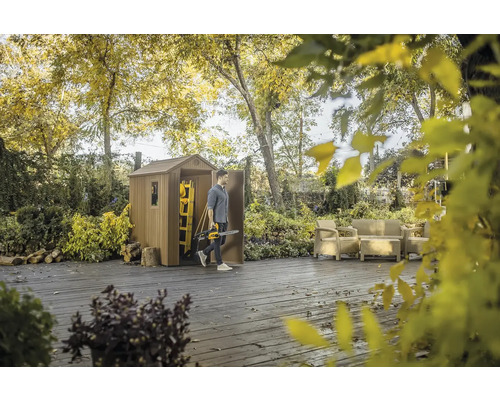 Záhradná scéna s domčekom na náradie, terasovým nábytkom a osobou s motorovou pílou.