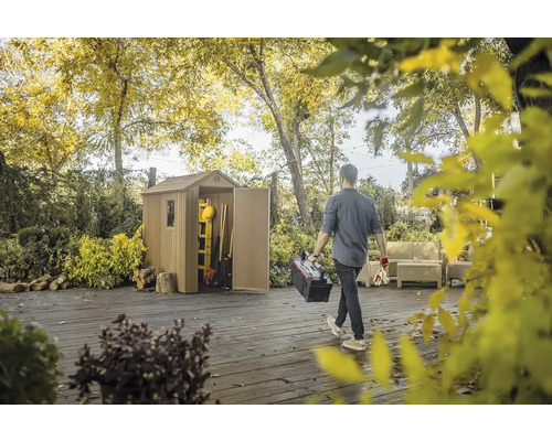 Scéna so záhradným domčekom v záhrade a osobou nesúcou debnu s náradím.