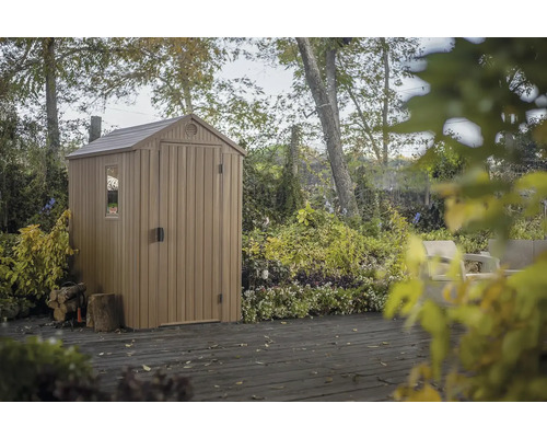 Plastový záhradný domček s oknom a dverami na drevenej terase, obklopený stromami a rastlinami.