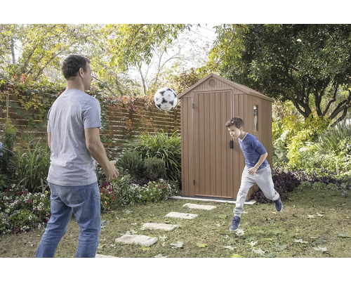 Otec a syn sa hrajú s futbalom pred záhradným domčekom v záhrade.