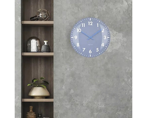 Modré nástenné hodiny s ciferníkom visia na sivej stene vedľa drevenej police.