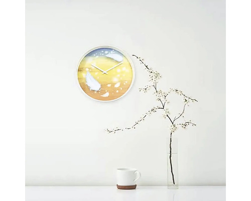 Nástenné hodiny s motívom peria vo svetlej miestnosti