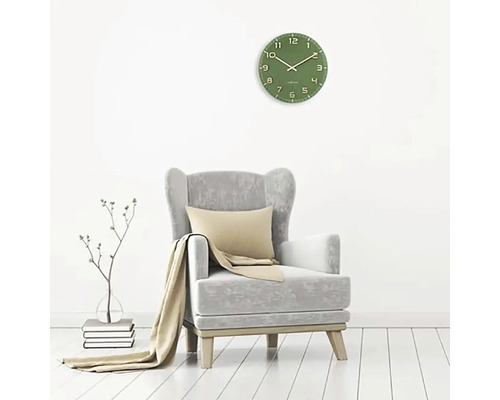 Obývacia izba so zelenými nástennými hodinami, kreslom, vankúšom a dekou.