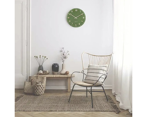 Obývacia izba so zelenými nástennými hodinami, kreslom a kobercom