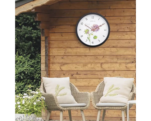 Záhradná scéna s nástennými hodinami na drevenej stene a dvoma ratanovými kreslami s vankúšmi