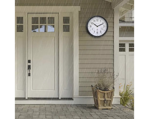 Scéna s okrúhlymi, poveternostným vplyvom odolnými vonkajšími hodinami vedľa vchodových dverí počas dažďovej prehánky.