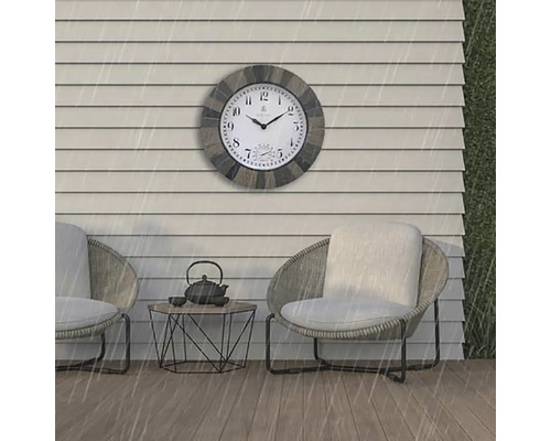 Vonkajšia scéna s nástennými hodinami odolnými voči poveternostným vplyvom nad dvoma kreslami a malým stolíkom