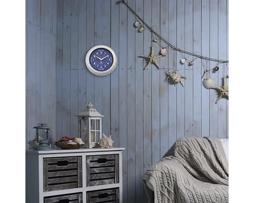 Dekoratívna obývacia izba s nástennými hodinami, komodou, lampášom, pohovkou a námornými dekoratívnymi prvkami, ako sú hviezdice a mušle.
