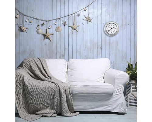 Obývacia izba s bielou pohovkou, pletenou dekou, nástennou dekoráciou s hviezdicami a mušľami a nástennými hodinami.